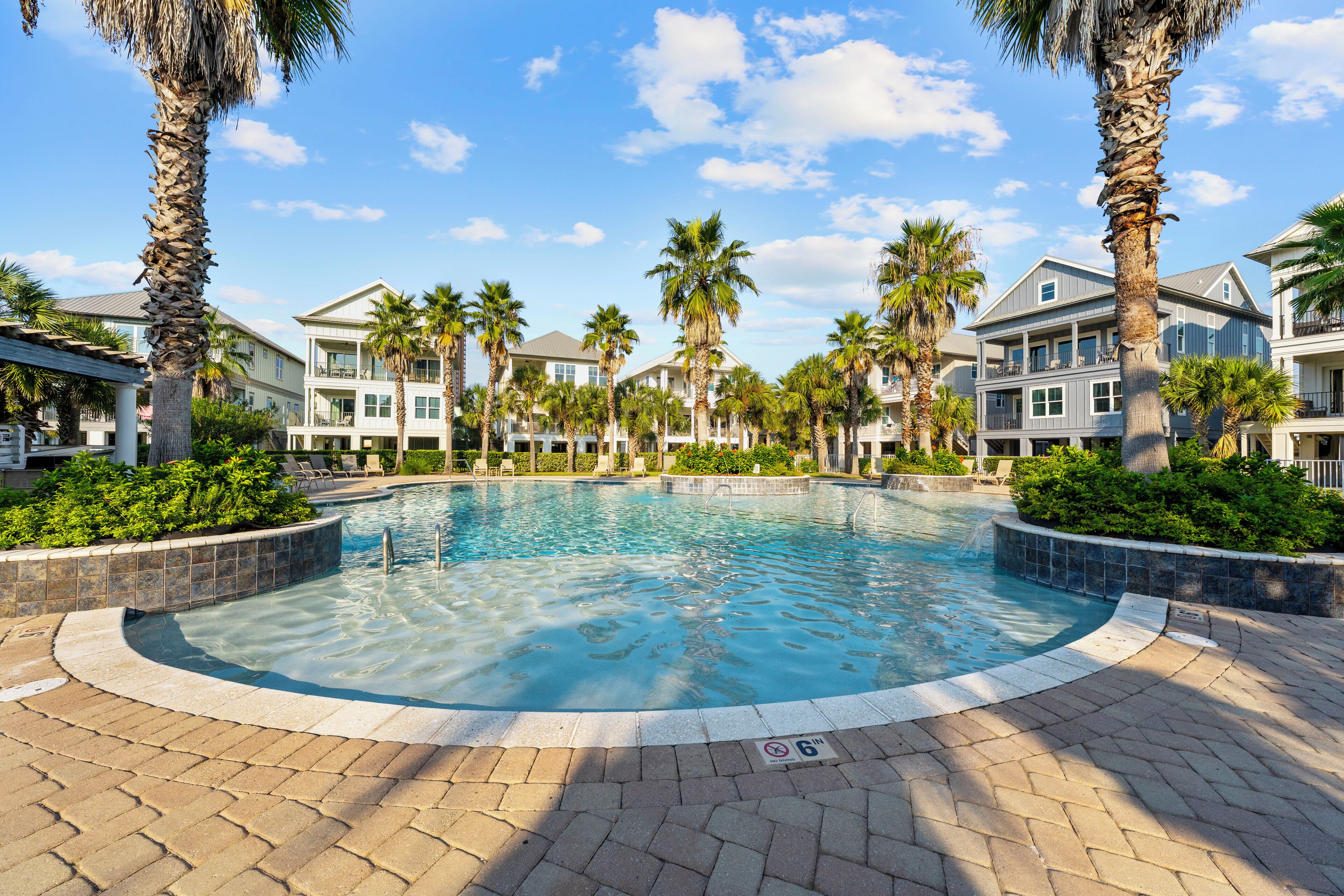 A swimming pool surrounded by palm trees and a brick walkway.