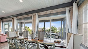 Une vaste terrasse dotée d’une table et de chaises en bois, de grandes fenêtres et d’un espace salon extérieur.