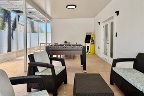 A covered patio area with a foosball table, wicker furniture, and a small table with chairs.