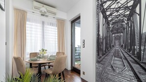 Comedor con una mesa dispuesta para cuatro personas, un ventanal con cortinas de gasa y un mural en la pared de una vía de tren.
