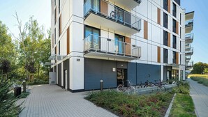 A modern multi-story residential building with balconies, a covered entrance, and a bike parking area.