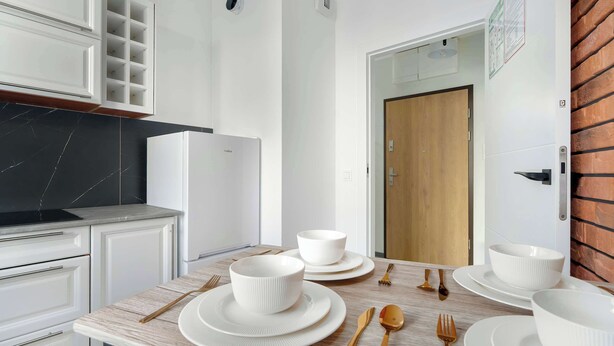 A modern kitchen with white cabinetry, a black marble countertop, and a wooden door.