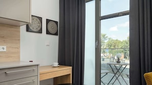 Et moderne værelse med skrivebord, stol, en lille skammel og udsigt til et udendørs område med bord og stole.