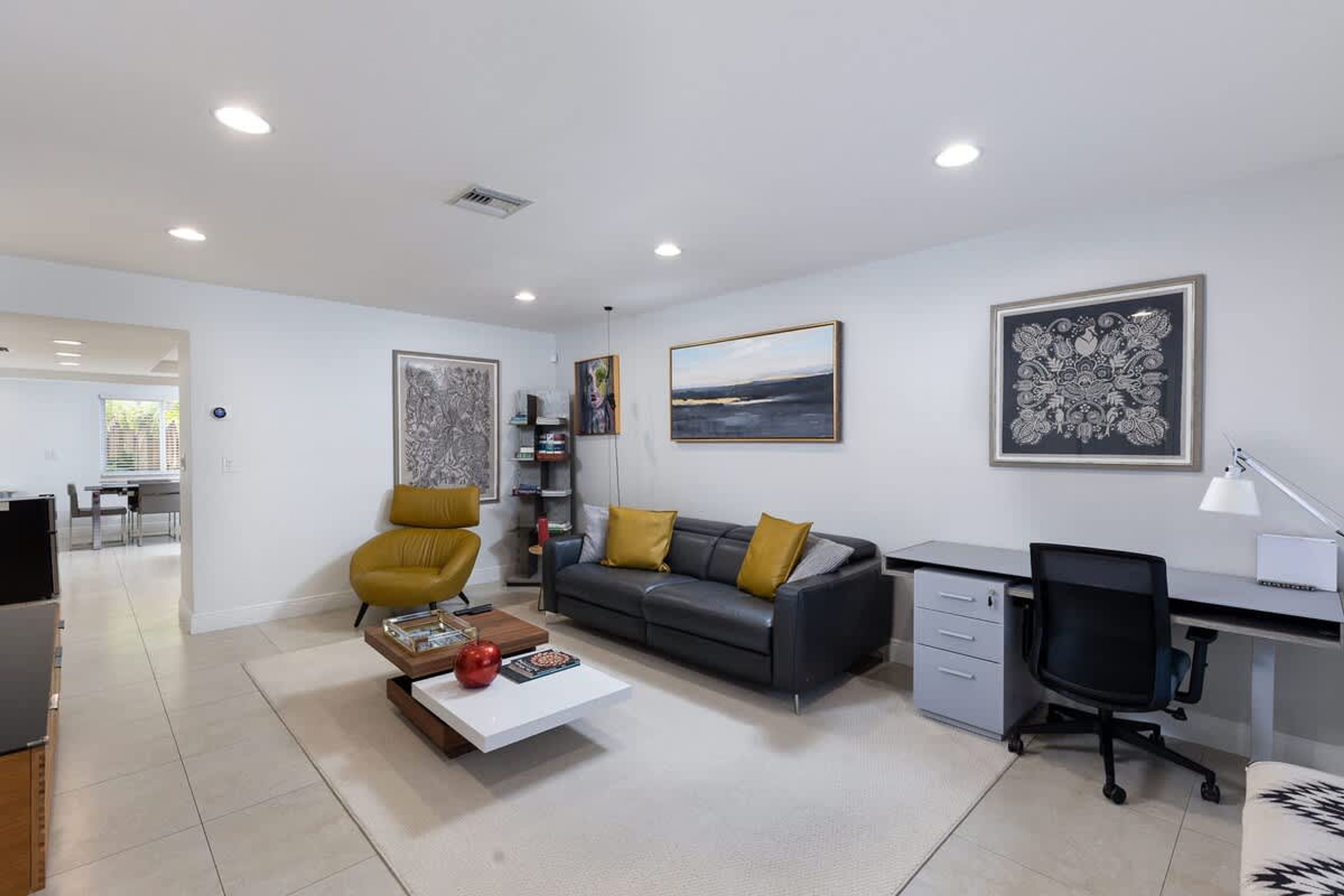 Un salon moderne avec un canapé gris, un fauteuil jaune et un bureau avec un ordinateur.