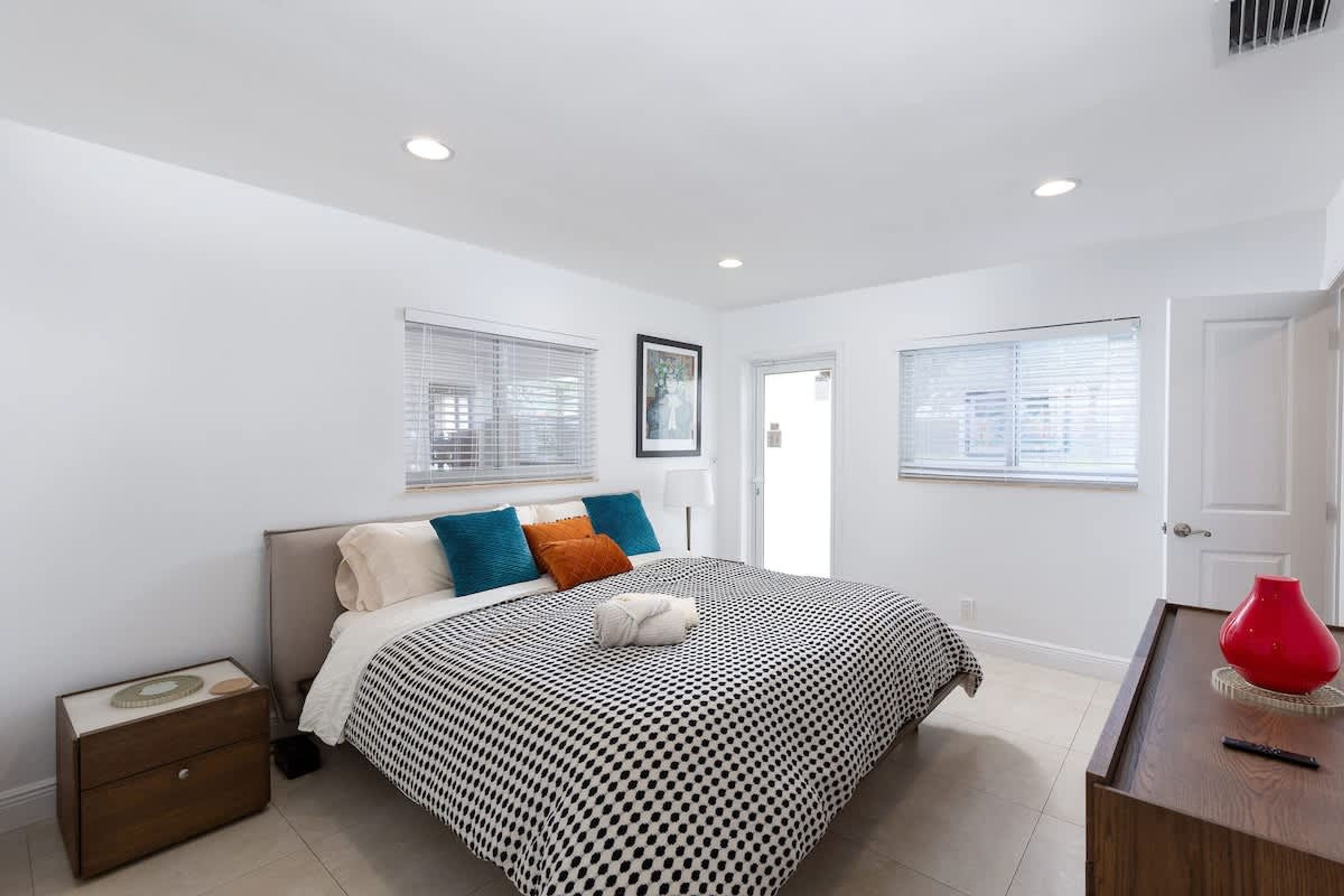 A bedroom with a bed, a nightstand, a dresser, and two windows with blinds.