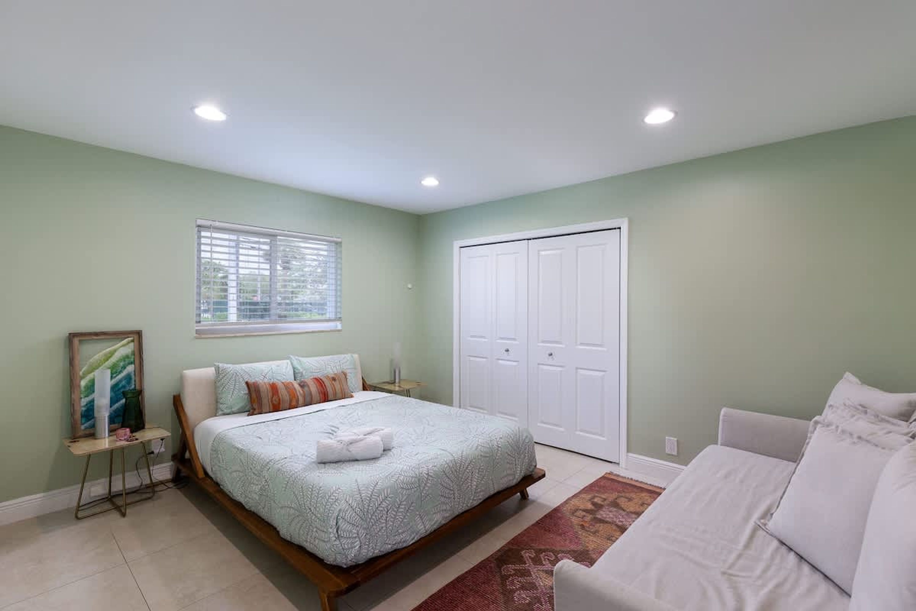 A bedroom with a bed, a nightstand, a window, and a closet.