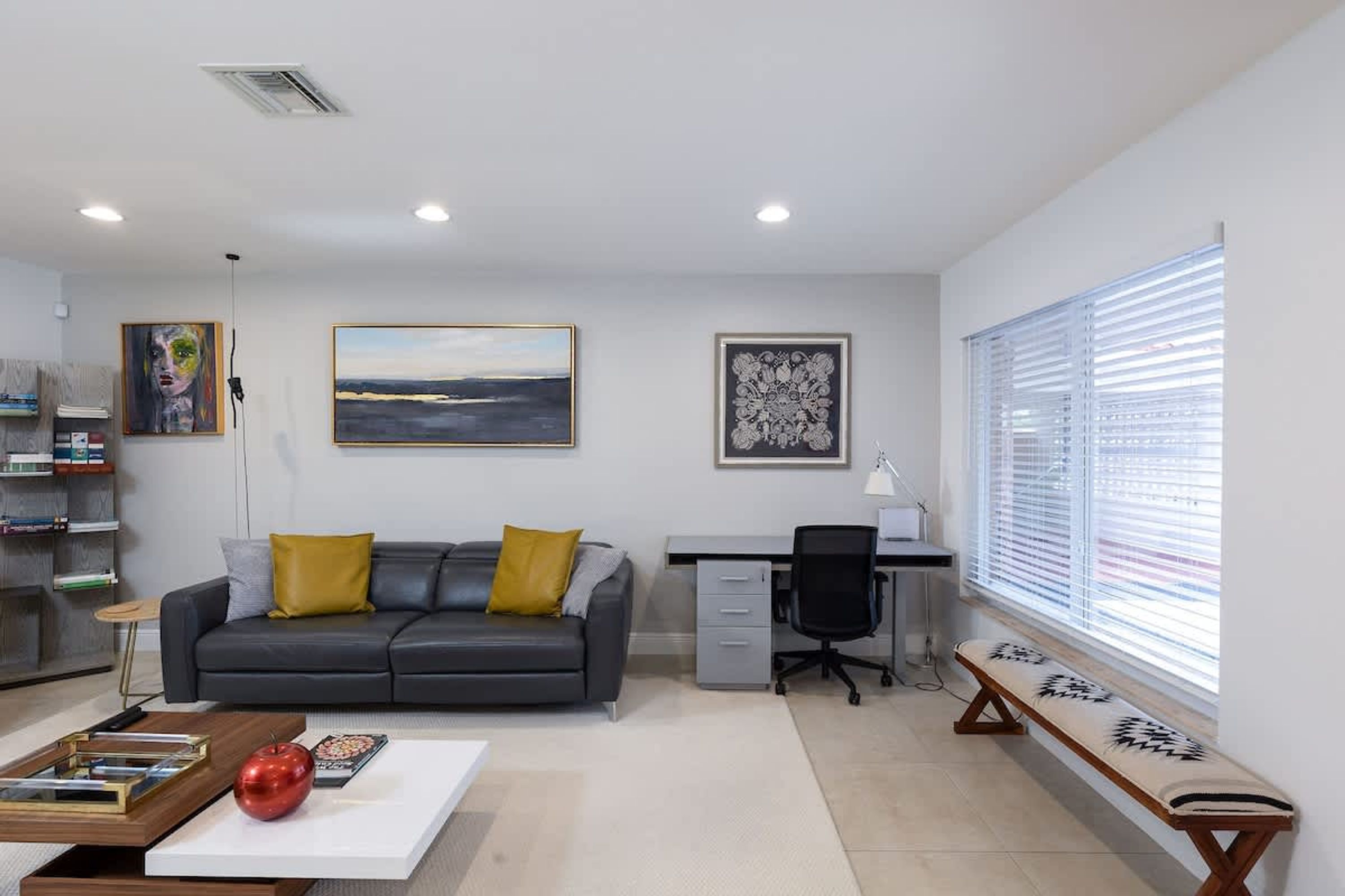 Un salon moderne avec un canapé gris, une table basse, un bureau avec une chaise et un banc près de la fenêtre.