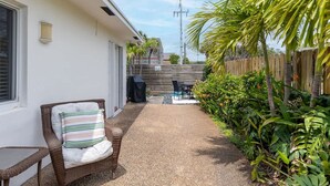 Un patio couvert comprenant une chaise en osier, une table et un barbecue.