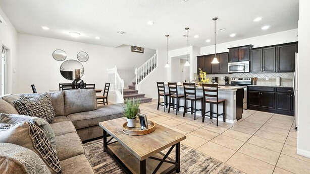 A spacious living room with a large sectional sofa, a wooden coffee table, and a dining area with a kitchen in the background. - Perfect Retreat with Incredible Resort! (Kissimmee)