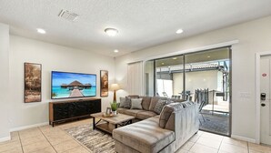 A living room with a sectional sofa, a coffee table, and a TV. There is a sliding glass door leading to an outdoor area. - Perfect Retreat with Incredible Resort! (Kissimmee)