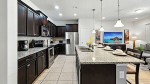 A modern kitchen with dark cabinets, granite countertops, stainless steel appliances, and pendant lighting. - Perfect Retreat with Incredible Resort! (Kissimmee)