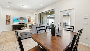 A modern living room with a dining area, a TV, and a sliding glass door leading to a balcony. - Perfect Retreat with Incredible Resort! (Kissimmee)