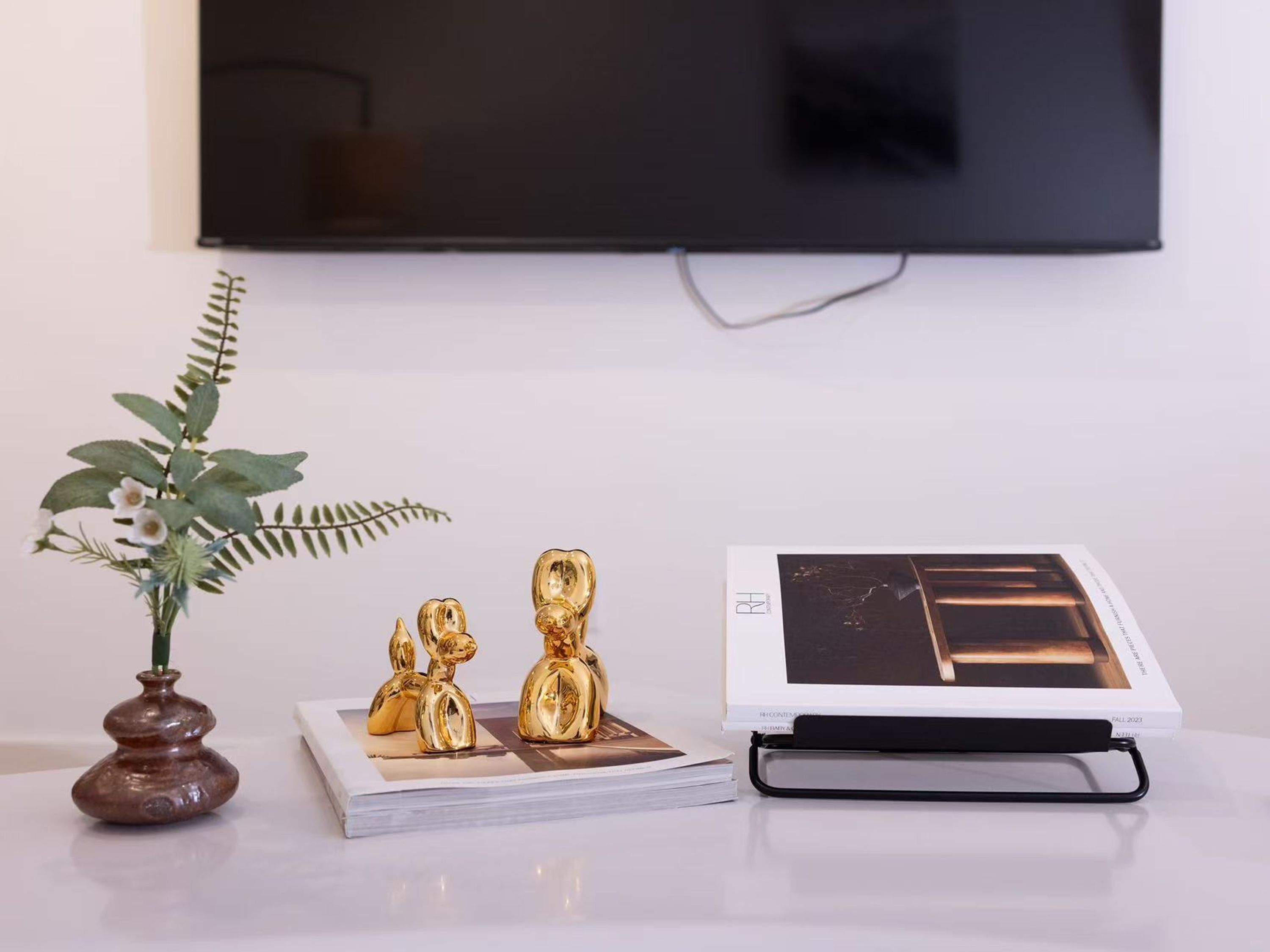A white table with a small potted plant, three golden figurines, and a book with a black cover.