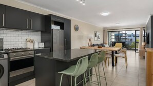 A modern kitchen with dark cabinets, a central island with bar stools, a refrigerator, and a dining area with a table and chairs.