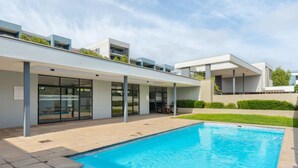 A modern building with a swimming pool, large windows, and a covered outdoor area.