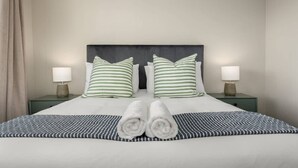 A neatly made bed with striped pillows and rolled towels, two bedside lamps, and a dark headboard.