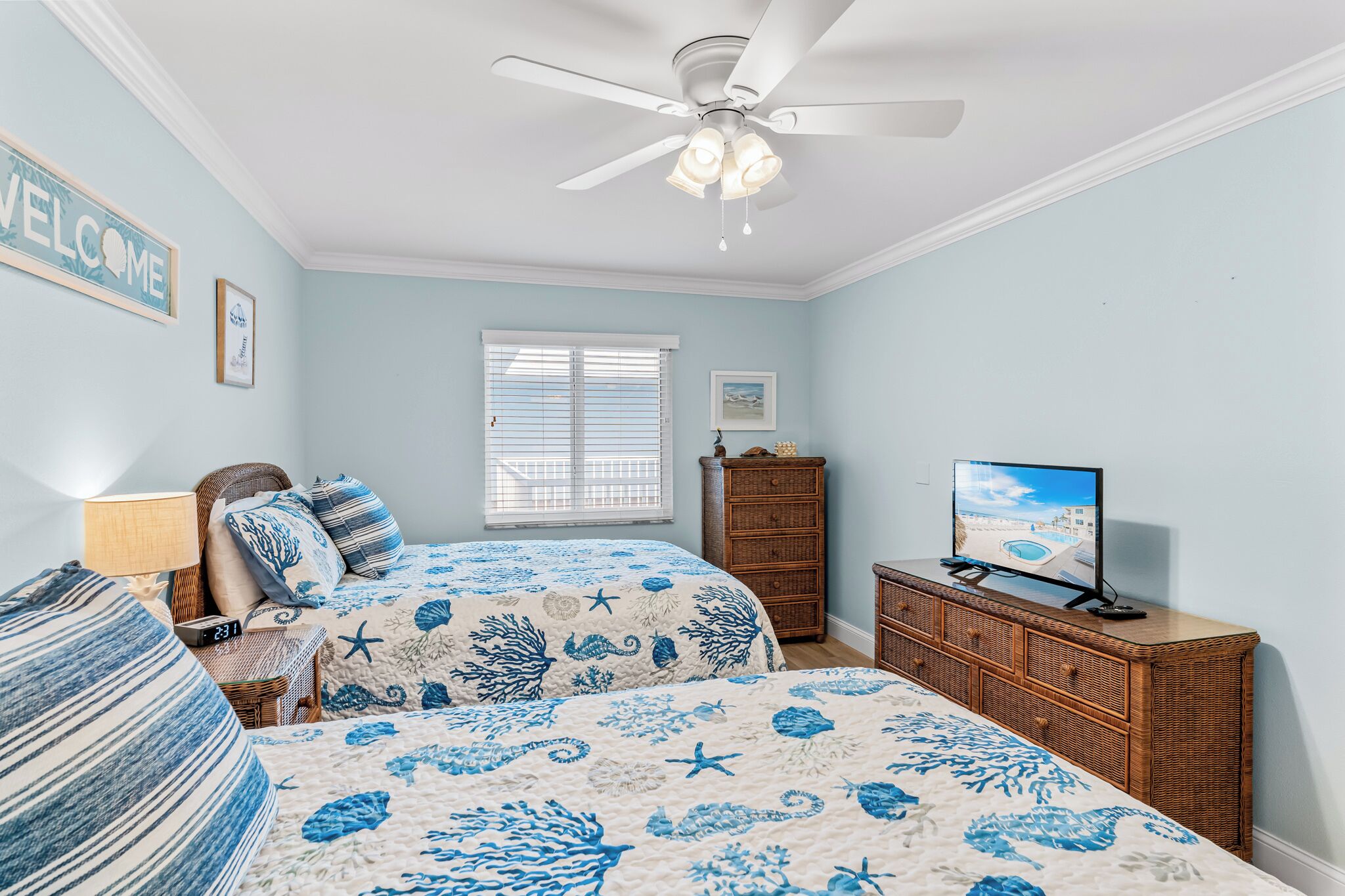A bedroom with two beds, a ceiling fan, a dresser, and a TV.
