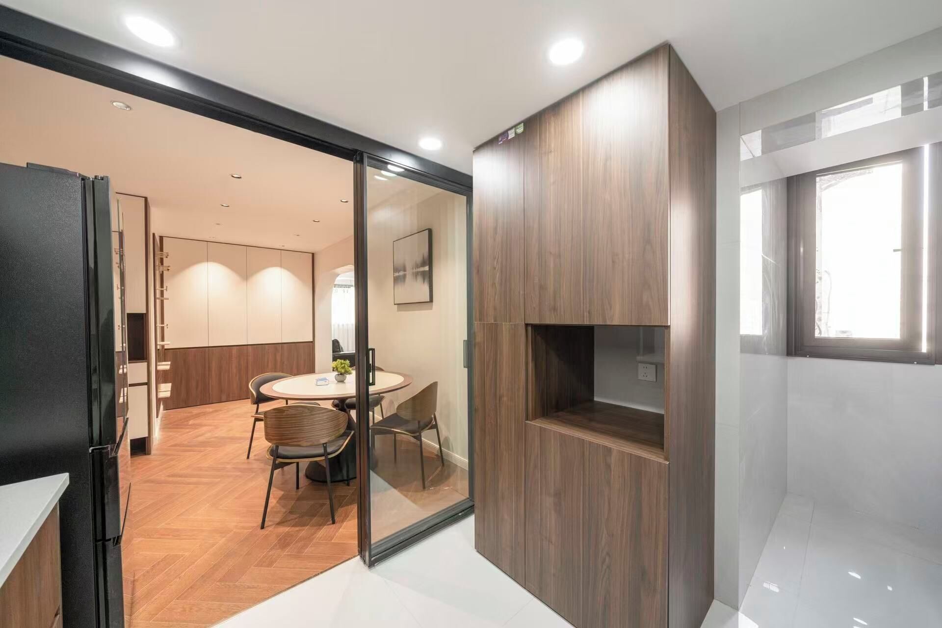 A modern interior with a wooden cabinet, a glass partition, and a dining area with chairs and a table.