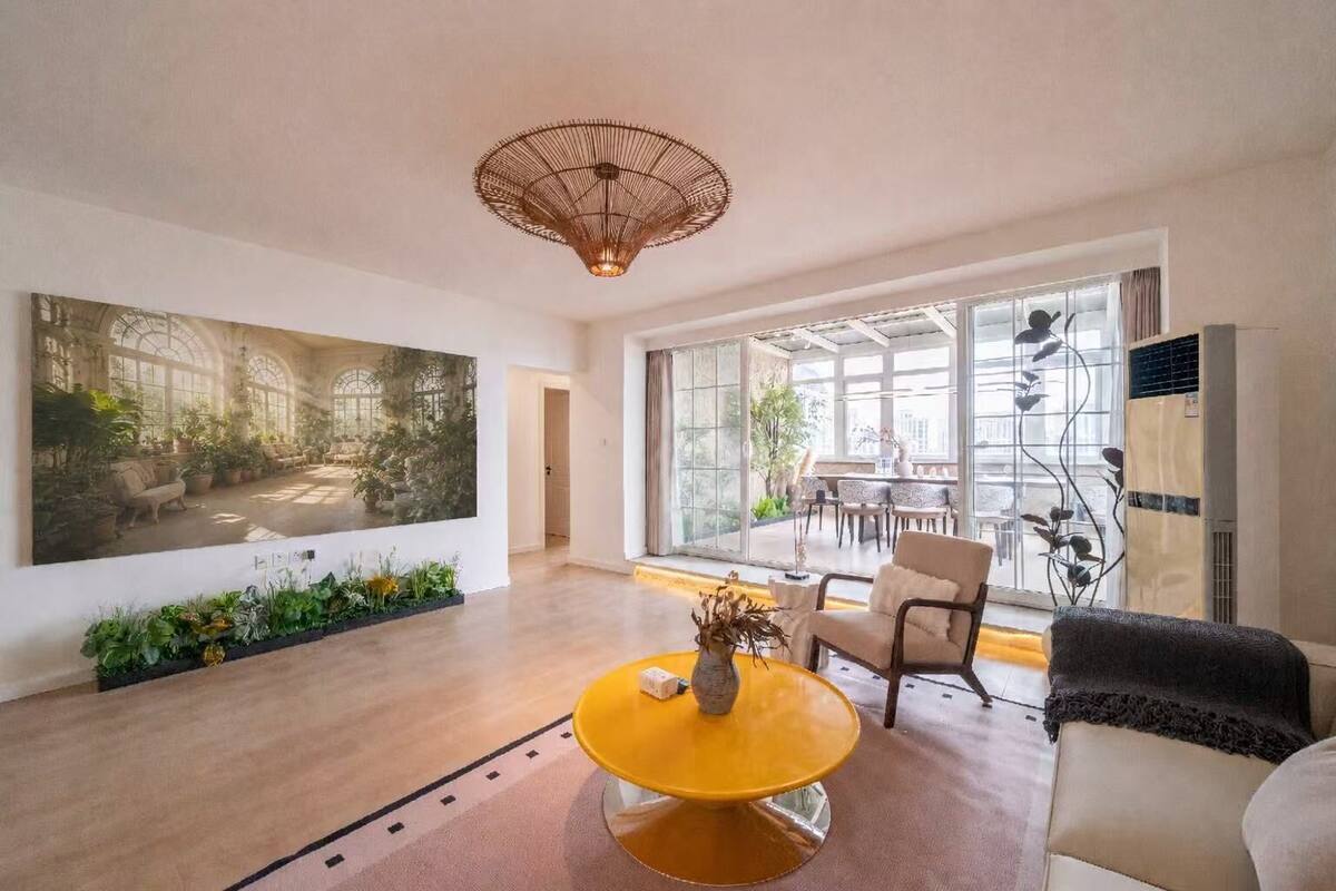 Un salón espacioso con un amplio ventanal, una mesa de centro amarilla y un moderno candelabro.