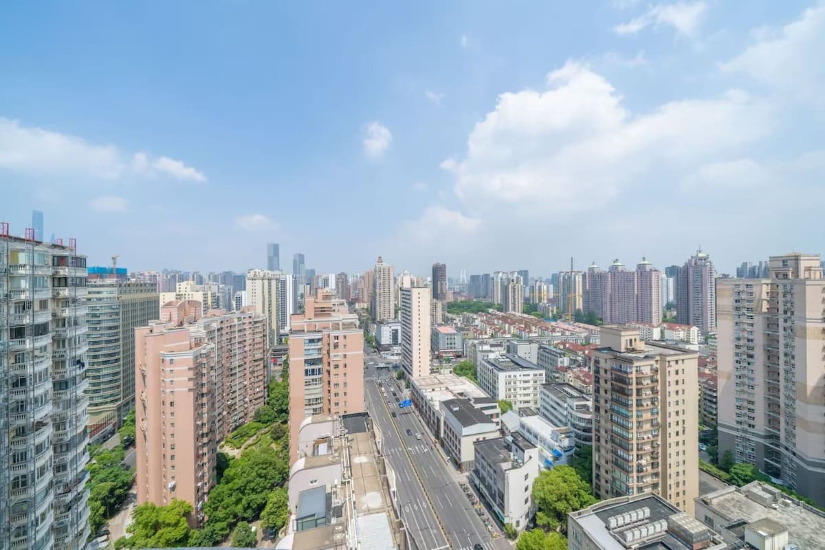 A cityscape with high-rise buildings, a wide road, and some greenery.