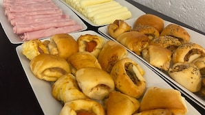 A buffet table with various food items including rolls, sausages, and sliced meats. - Pousada Jardim das Estações (Itatiaia)