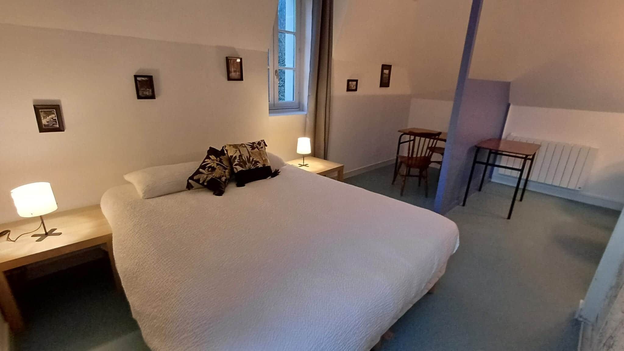 Un dormitorio ordenado con una cama grande, mesitas de noche con lámparas, un escritorio pequeño y un radiador.