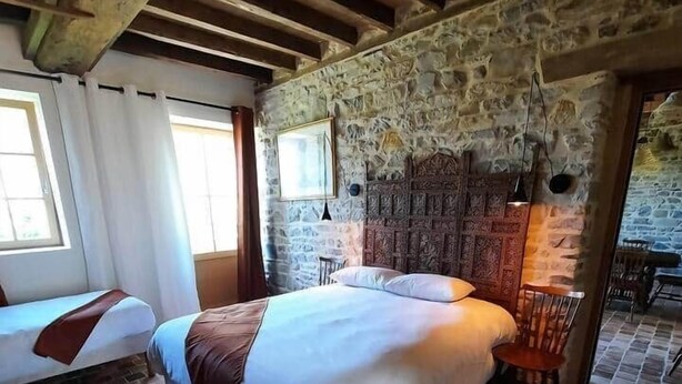Un dormitorio con pared de piedra, techo de madera y suelo de ladrillo.