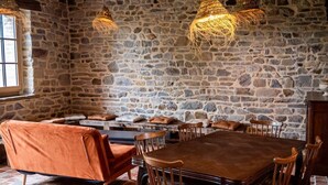 Una habitación con paredes de piedra, una mesa y sillas de madera, un sofá y lámparas de fibra.