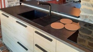 Una cocina con pared de piedra, un lavamanos negro y armarios de madera.