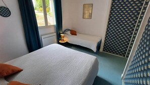 Un dormitorio con dos camas, una mesita de noche con lámpara, una ventana con cortinas y una pared con textura.