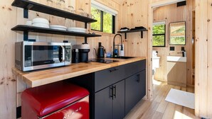 Una cocina compacta con microondas, cafetera y un electrodoméstico rojo, paredes de madera y una ventana.