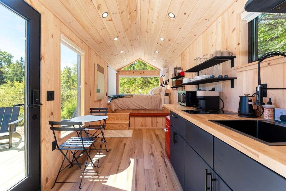 A compact wooden cabin with a kitchenette, a dining area, and a bed.