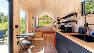 A compact wooden cabin with a kitchenette, a dining area, and a bed.