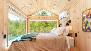A wooden cabin bedroom with a bed, a window, and an air conditioning unit.