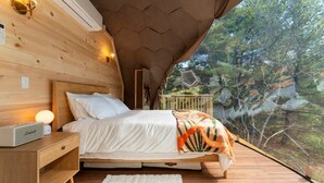 Une chambre à coucher avec un lit, une table de chevet, une lampe et une vue sur les arbres par la fenêtre.