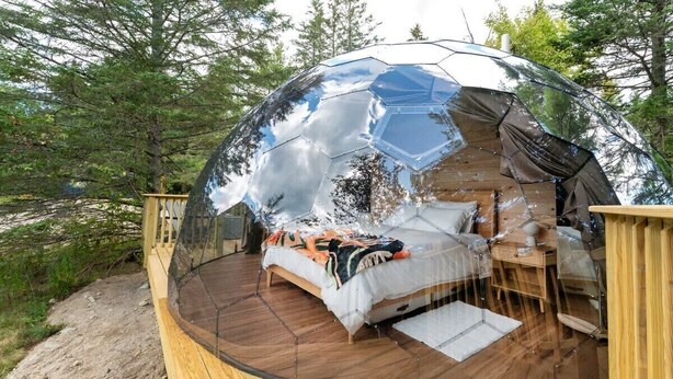 Une structure en forme de dôme sphérique en verre, comprenant un lit et une terrasse en bois.