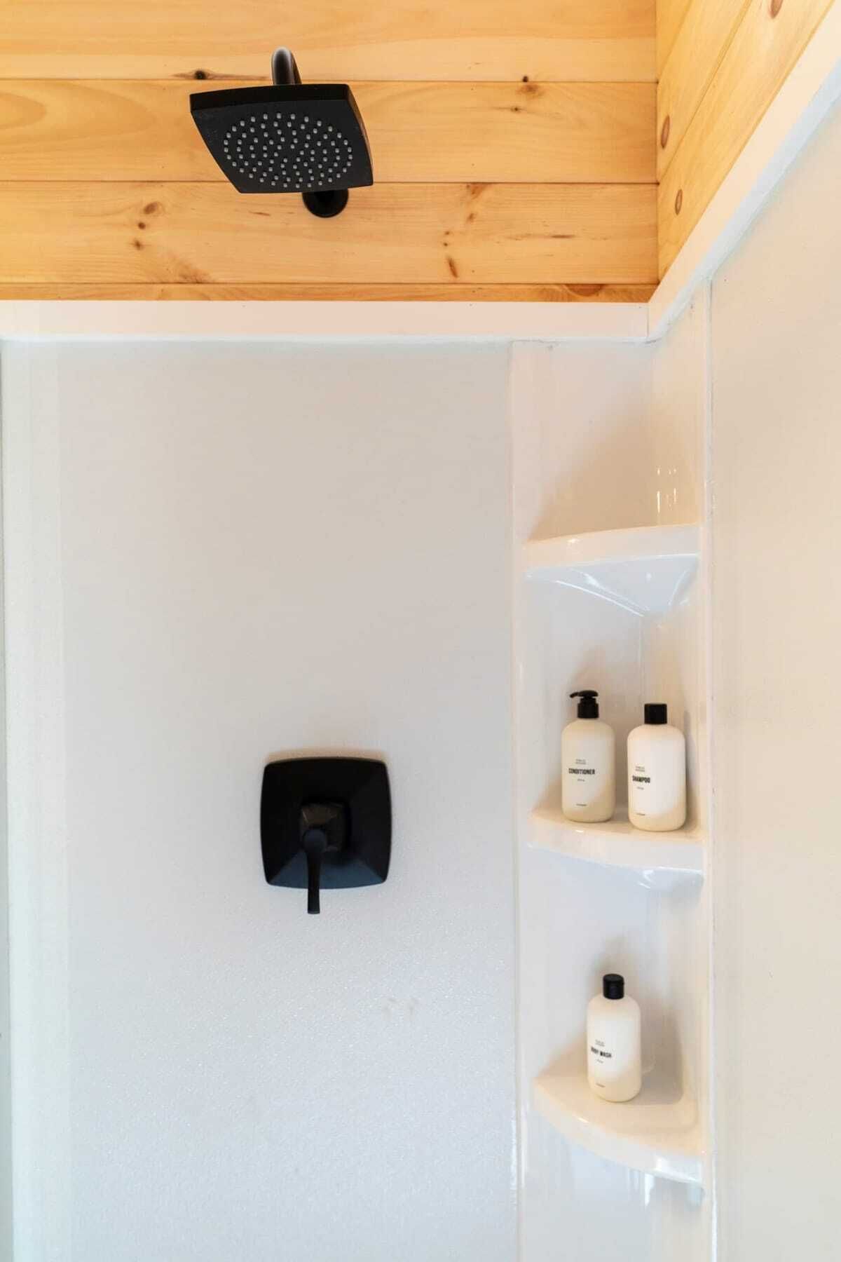 A shower with a handheld showerhead, a control panel, and three shelves with toiletries.