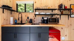 A compact kitchen with a sink, black cabinets, a red appliance, and wooden walls. - Vesta Nook! With Shower, Queen Bed & pullout sofa (Sullivan)