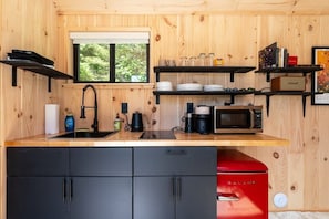 A compact kitchen with a sink, black cabinets, a red appliance, and wooden walls.