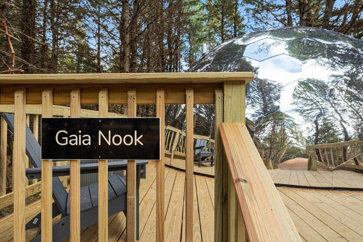 A wooden deck with a sign reading 'Gaia Nook' surrounded by trees.