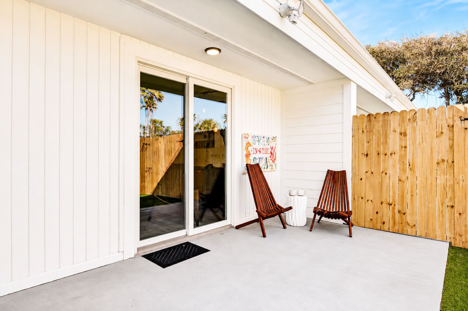 Un patio couvert avec une porte-fenêtre coulissante, deux chaises en bois et une clôture en bois.