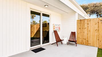 Un patio couvert avec une porte-fenêtre coulissante, deux chaises en bois et une clôture en bois.