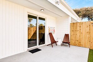 Un patio techado con puerta corrediza de vidrio, dos sillas de madera y cerca de madera.
