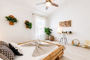 A modern bedroom with a bed, bedside table, lamp, and decorative plants.