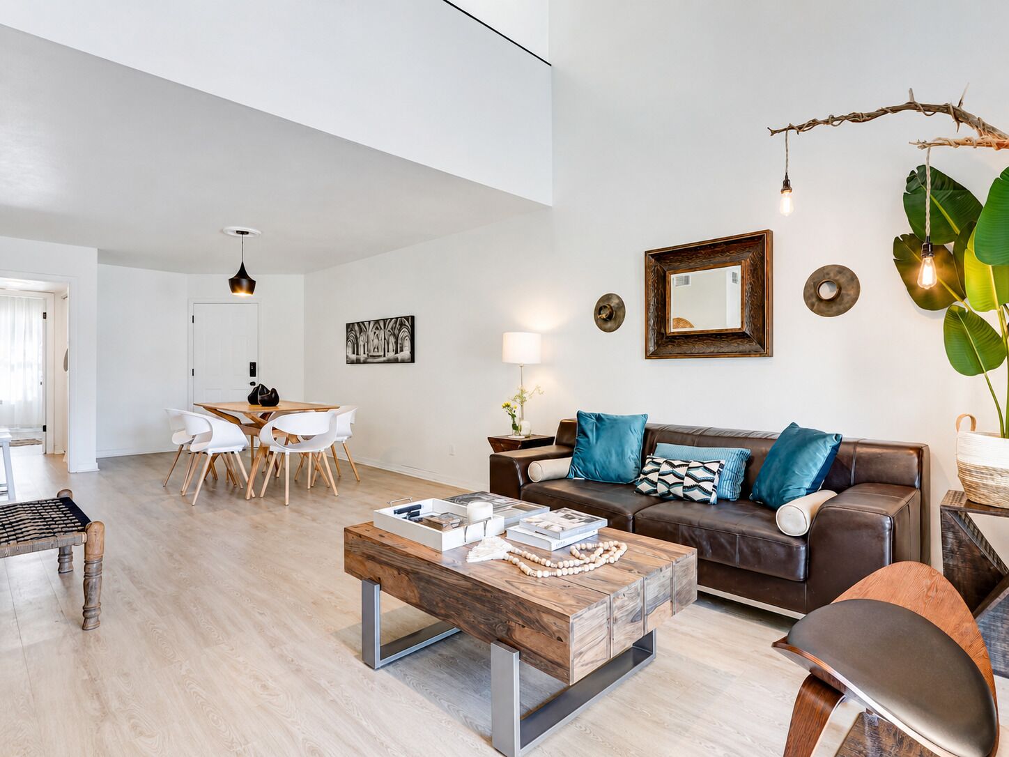 A modern living room with a wooden coffee table, a brown leather sofa, and a dining area with white chairs.