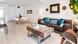 A modern living room with a wooden coffee table, a brown leather sofa, and a dining area with white chairs. - Classy Bohemian Beach Cabana- Close to Beach (St. Augustine)