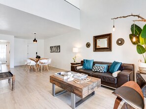 Een moderne woonkamer met een houten salontafel, een bruine leren bank en een eethoek met witte stoelen.