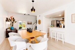 A modern kitchen with white cabinetry, a wooden dining table, and white chairs.