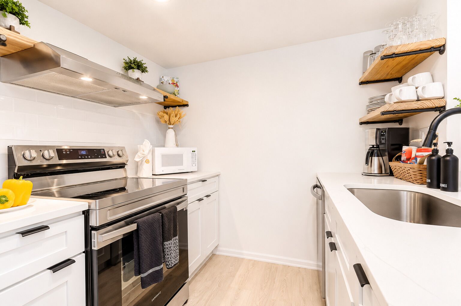 A modern kitchen with stainless steel appliances, white cabinetry, and wooden shelves.