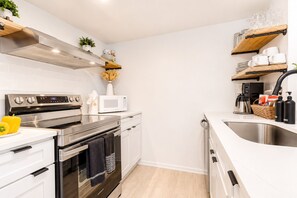 Een moderne keuken met roestvrijstalen apparatuur, witte kasten en houten planken.